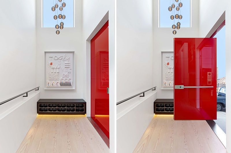 A bright red, glossy pivoting door that was fabricated in Italy, welcomes visitors to this modern house. #RedFrontDoor #FrontDoor #ModernHouse #Entryway