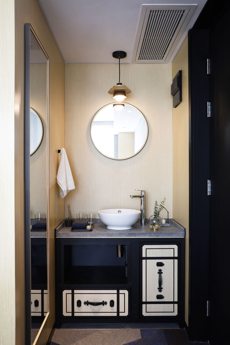 This modern hotel bathroom features a black vanity with a concrete countertop and a simple round mirror. #HotelBathroom #BathroomInspiration #BathroomIdea #ModernBathroom