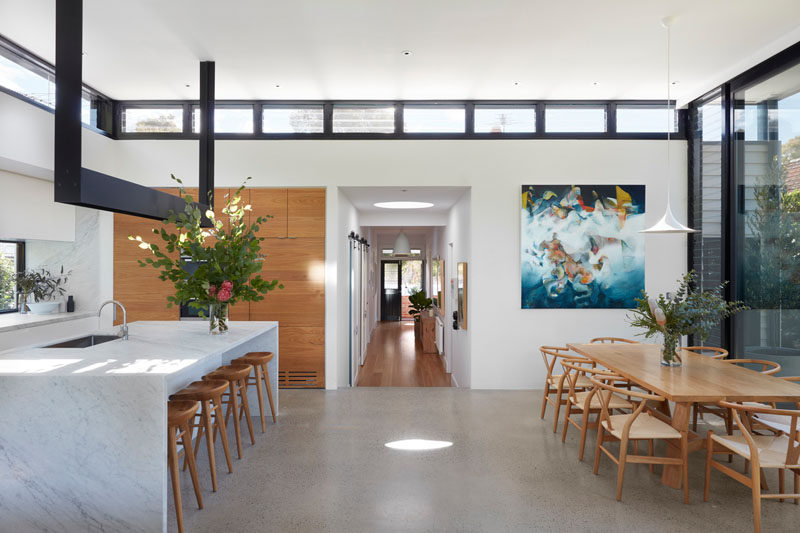 The hallway in this renovated house opens up to the new extension, where the flooring transitions from floorboard to polished concrete, and clerestory windows filter more light through to the new social areas of the home. #ConcreteFlooring #ModernHouseExtension #ClerestoryWindows #InteriorDesign