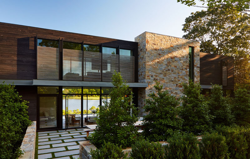 Upon arriving at this modern house, there's an patio with an outdoor dining area that's surrounded by plants. #Landscaping #ModernHouse #Architecture