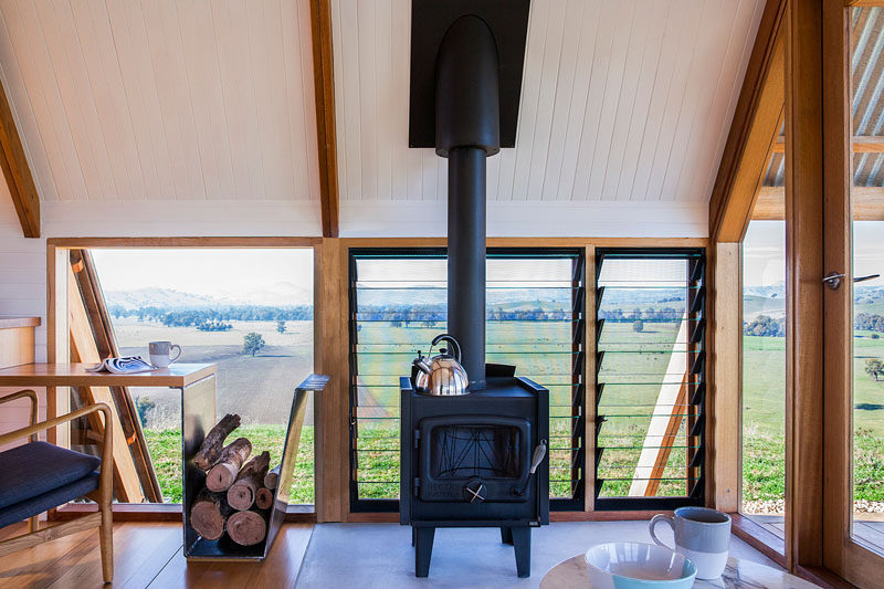 A black freestanding wood burner fireplace keeps the interior of this cabin warm on a cool night, while louvre windows allow for airflow on a warm day. #Fireplace #LouverWindows #FirewoodStorage