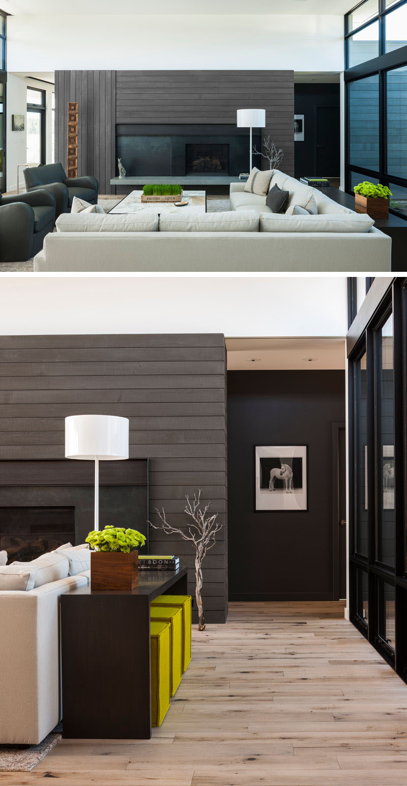 This modern living room features a stained cedar wood accent wall surrounds a black fireplace, while a light colored couch, high ceilings and plenty of windows help to keep the interior bright. #StainedCedar #LivingRoom #InteriorDesign