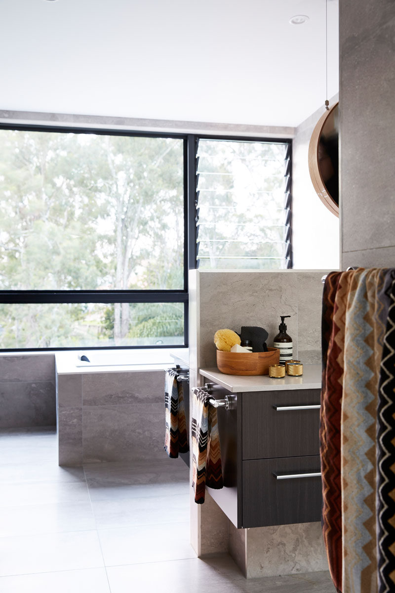 In this modern master bathroom, a pony wall creates a divide between the two sides of the vanity, while the built-in bathtub sits below the window. #Bathroom #ModernBathroom #BathroomDesign