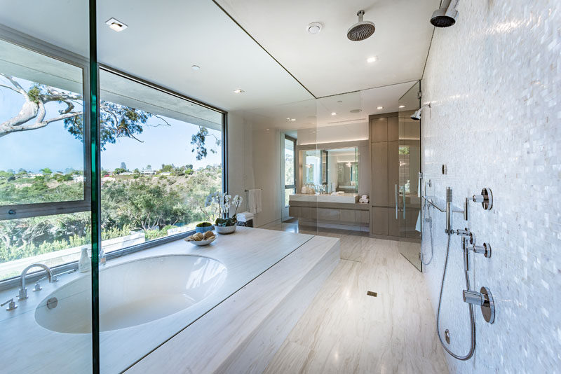 In this modern master bathroom, there's a built-in bathtub positioned in front of the windows, while a rainfall shower is positioned next to it. #MasterBathroom #EnsuiteBathroom #BuiltInBathtub