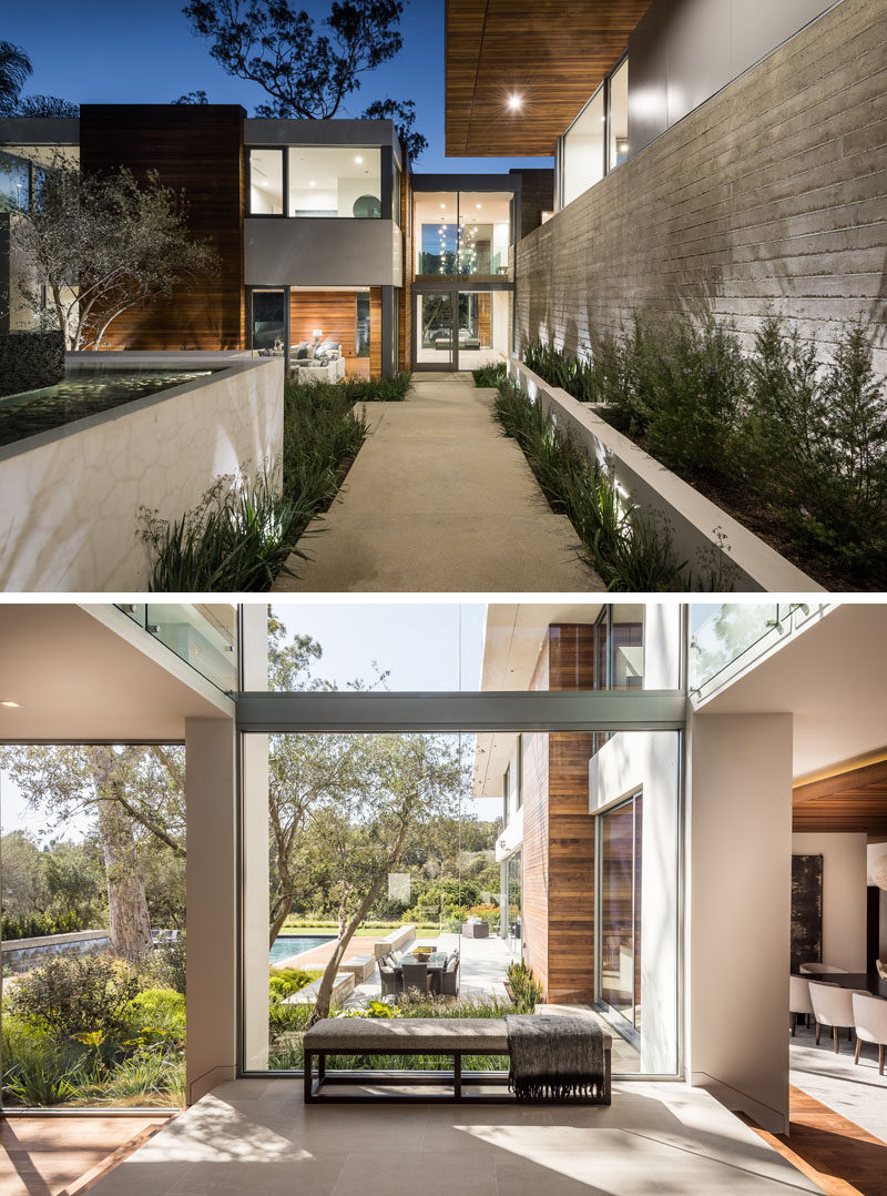 At the front of this modern house, a path that's positioned between a board-form concrete wall, and a cascading garden and fountain, leads to the front door and through to the foyer with views of the backyard. #Foyer #Landscaping #Concrete #Entryway