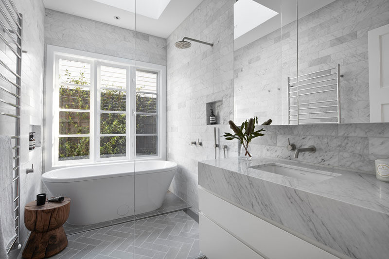 In this modern bathroom, floor-to-ceiling grey tiles have been installed and a freestanding bathtub was added in front of the windows. #ModernBathroom #GreyBathroom #FreestandingBathtub