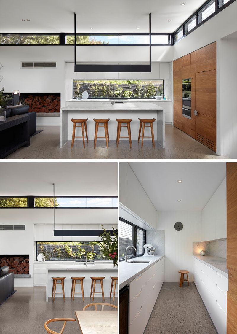 In this modern white kitchen, a window with views of the garden has been used as a backsplash, while hidden behind a wooden door at the end of the counter opens to reveal a hidden walk-in pantry with plenty of storage. #ModernKitchen #WhiteKitchen #WalkInPantry #Pantry