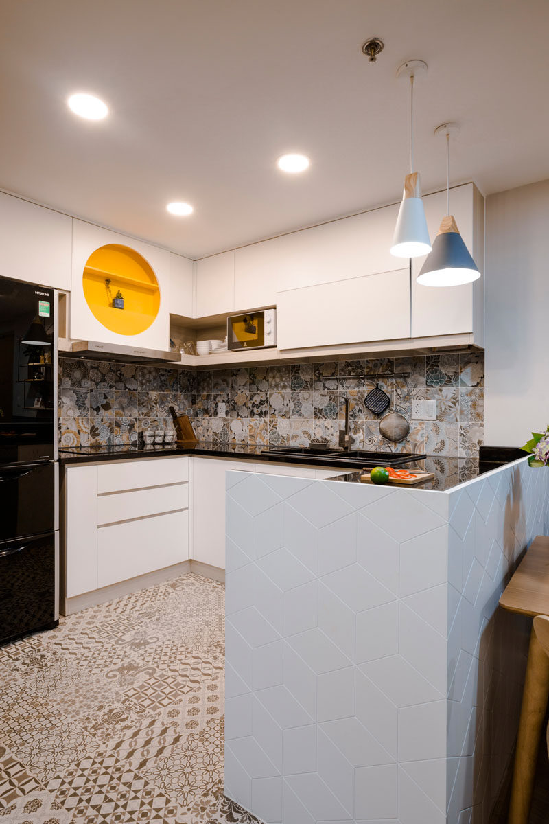 In this contemporary kitchen, the floor has been raised to separate it from the living area, and encaustic tiles cover the floor and backsplash. White cabinets were used to help make the kitchen feel larger. Click through to see more photos of this apartment. #WhiteKitchen #ModernKitchen #PatternedTiles #KitchenDesign