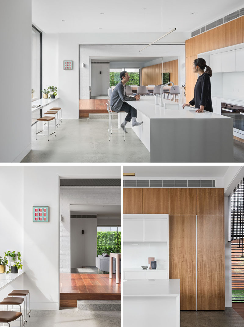 In this modern kitchen, a large white island creates plenty of counter space, while facing the window is a counter with stools, that allows people to relax and look outside. The kitchen also features integrated joinery with a concealed fridge. #ModernKitchen #WhiteKitchen #LargeKitchenIsland