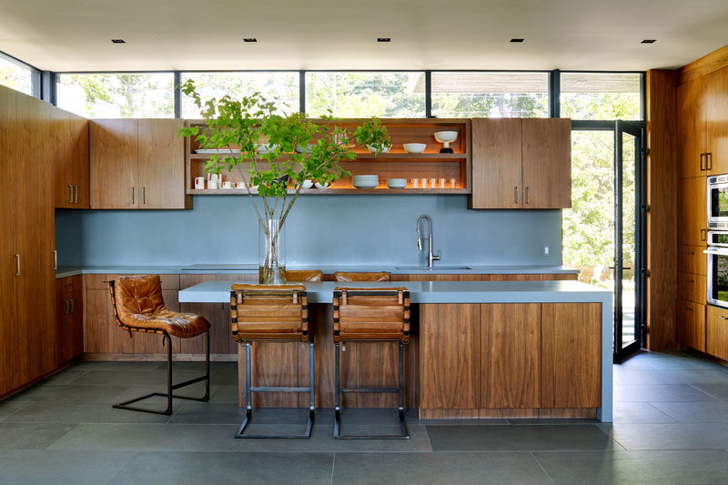 This modern kitchen has soft blue countertops and backsplash, with wood cabinetry and open shelving with lighting. #BlueCountertops #WoodCabinets #KitchenDesign #ContemporaryKitchen