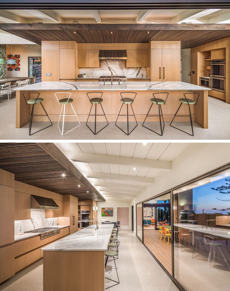 In this modern kitchen, there's a wood slat ceiling, and pantry doors sit flush within a full height hallway of wood cladding. A large island, with space for six people to sit at, ensures there's always plenty of seating when entertaining.