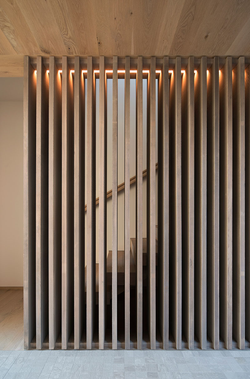 A wood slat partition with hidden lighting wraps around the stairs that lead to the upper floor of this home. #WoodPartition #WoodSlats #WoodSlatPartition