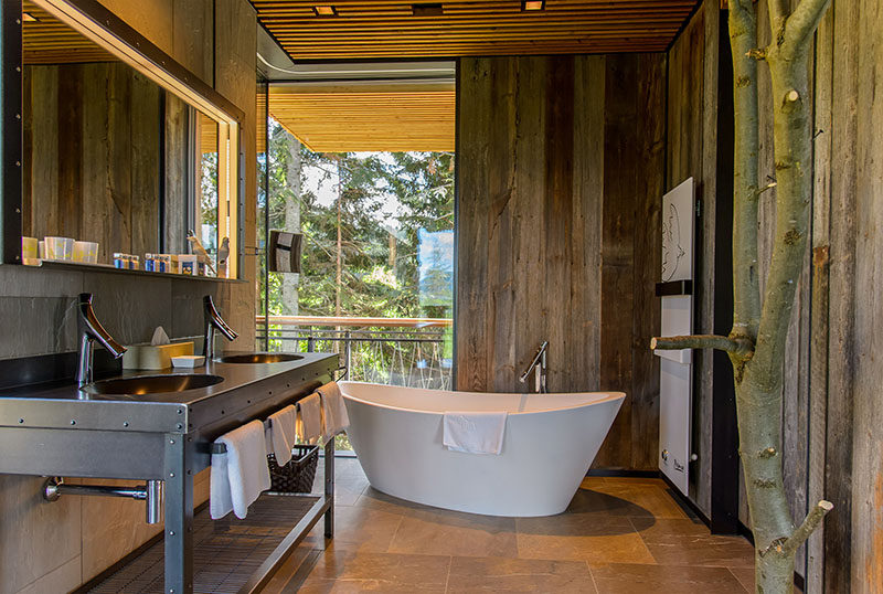 In this rustic modern bathroom, the freestanding bathtub is positioned to look out towards the trees through the floor-to-ceiling corner windows. #RusticModern #Bathroom #Windows #Bathtub