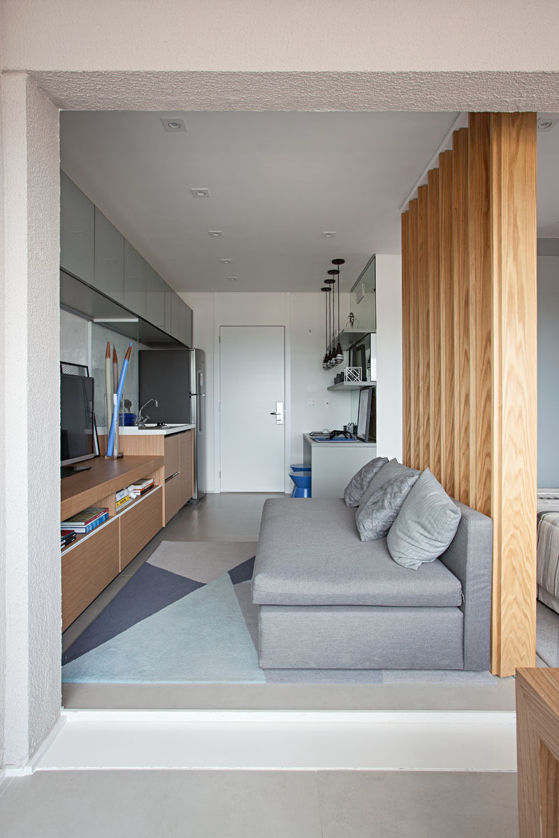 In this small apartment, a small grey couch is positioned opposite the television, and a geometric rug adds softness to the floor, while a wood slat wall separates the living room from the bedroom. #SmallApartment #InteriorDesign #LivingRoom