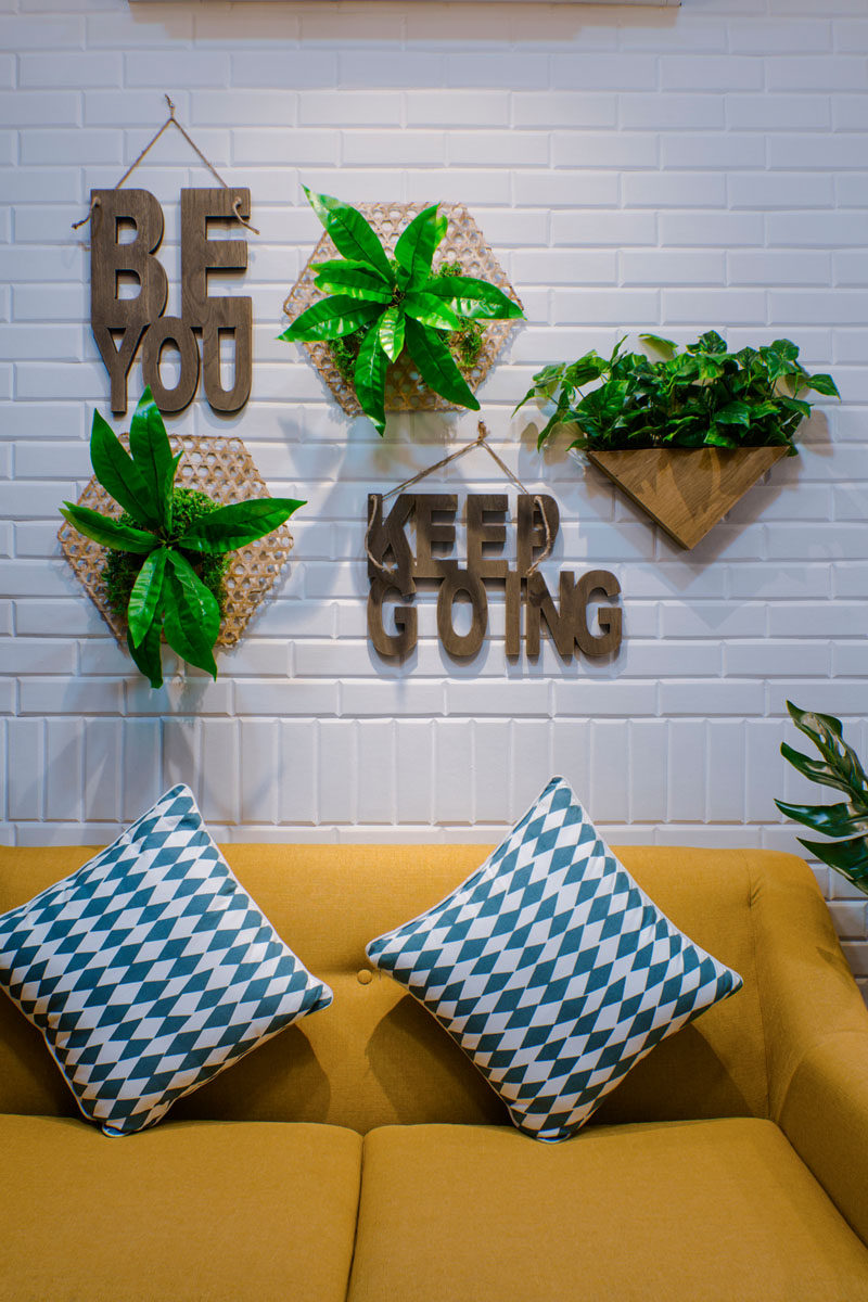 This modern living room features a painted white brick wall, wall plants, a yellow couch, patterned blue cushions and wood wall sayings. Click through to see more photos of this apartment. #LivingRoom #WallDecorIdeas #WallDecor #InteriorDesign