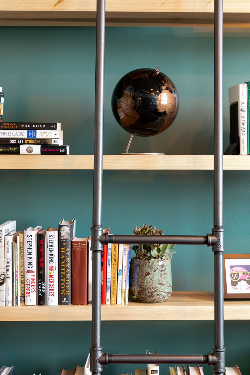 Francis Dominguez has transformed a spare empty bedroom into a library that features wood shelves, a metal ladder, and a reading area. #IndustrialModern #Library #InteriorDesign