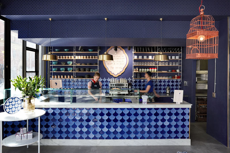 This cafe service area features blue feather-shaped ceramic tiles to create a handcrafted and detailed finish. #BlueTiles #InteriorDesign #CafeDesign #RetailDesign