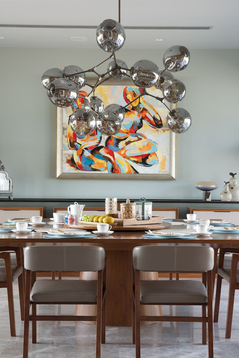 In this contemporary dining room, a large metallic chandelier hangs above a wooden dining table, while artwork brings in a touch of color to the room. #DiningRoom #InteriorDesign