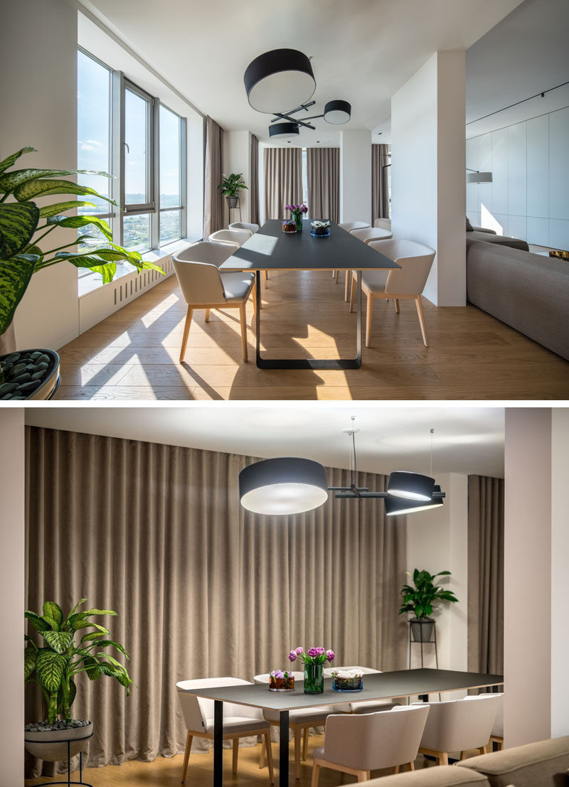 A minimalist dining table sits below a chandelier with drum shades, while a window provides views of the city. #DiningRoom #ModernDining