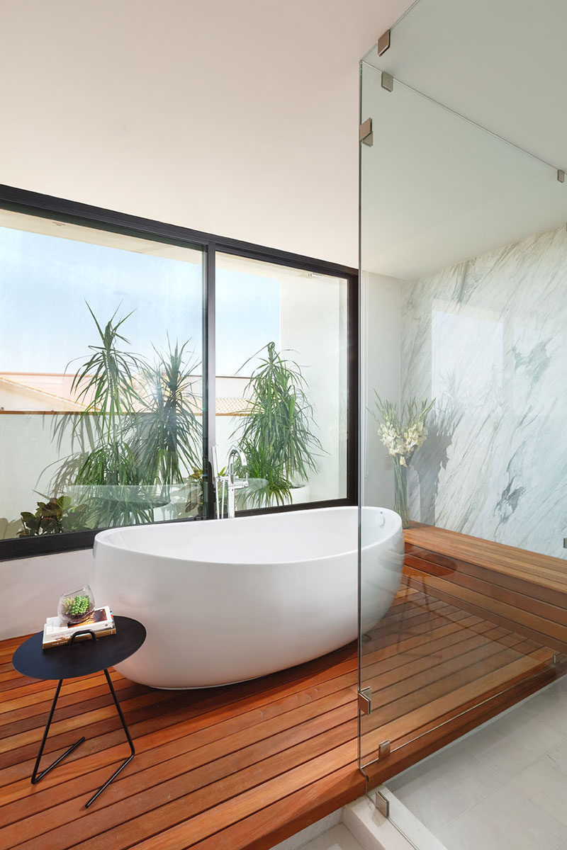 In this modern bathroom, a freestanding white bathtub is positioned in front of the window on a raised wood platform.