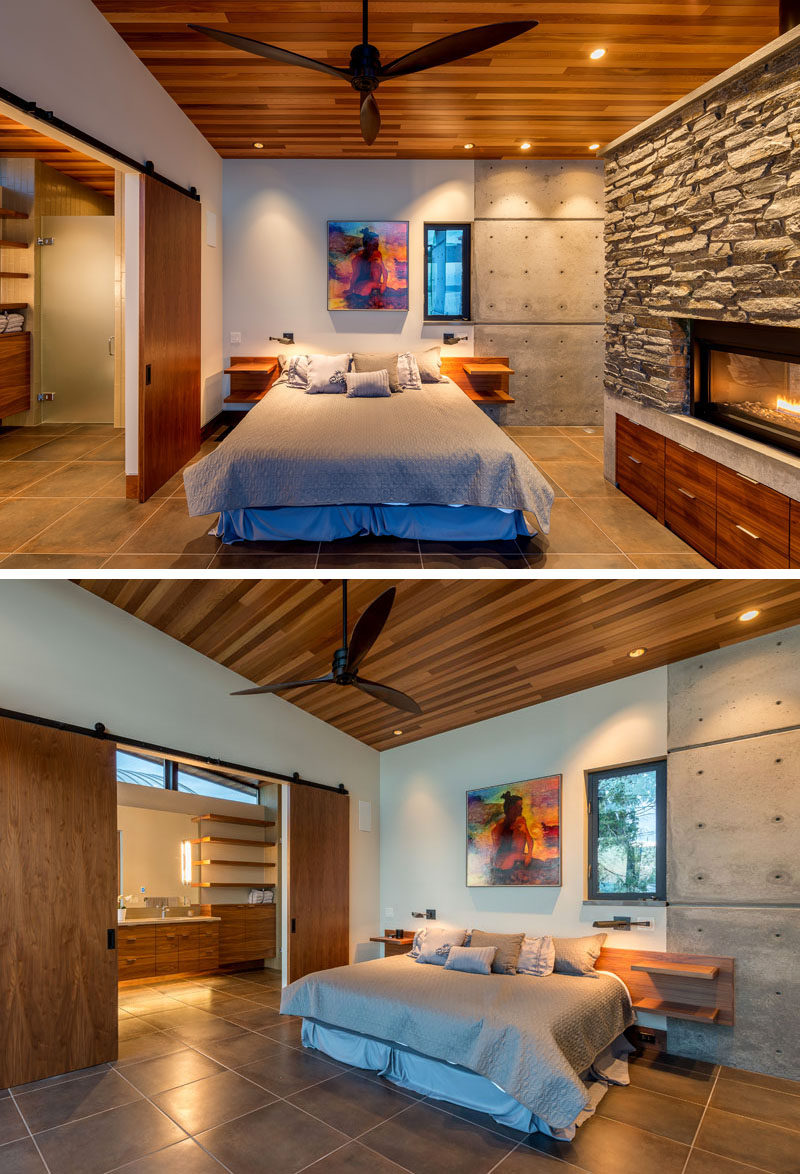 A set of sliding barn doors separate the bathroom from the bedroom, that features a stone, concrete and wood fireplace. #Bedroom #Fireplace #Doors