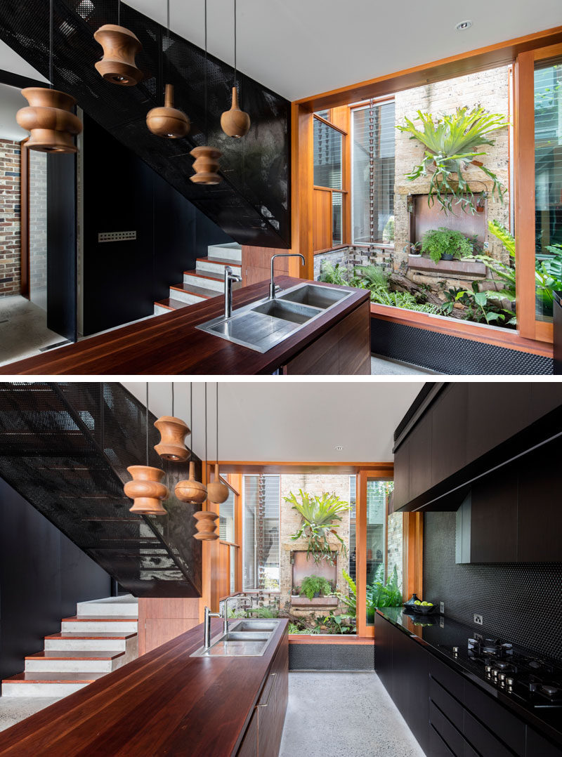 This modern black and wood kitchen has a view of a small courtyard. #BlackKitchen #BlackAndWood #InteriorDesign #ModernKitchen