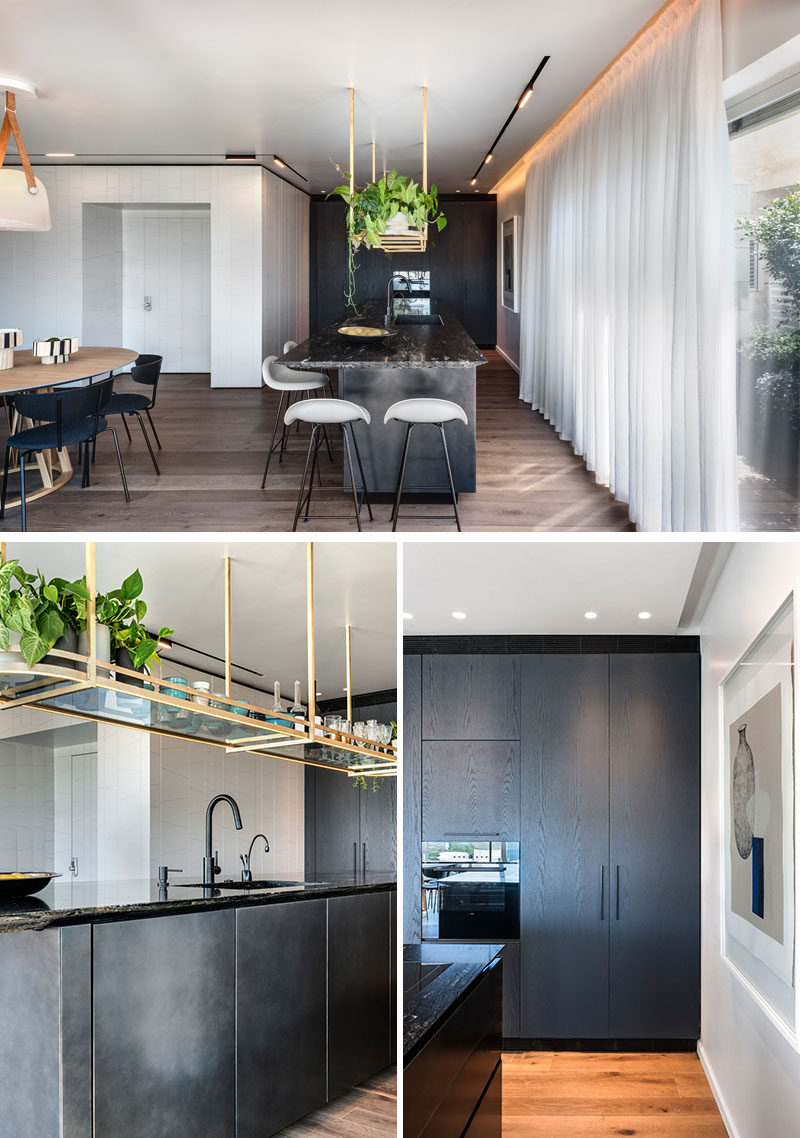 This modern kitchen features dark cabinetry, and a brass rack that hangs from the ceiling provides a place to display plants and decorative items. #ModernKitchen #BlackKitchen #KitchenDesign