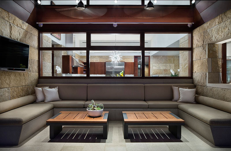 This modern house has an outdoor lounge filled with seating, and windows that provide a view of the kitchen inside. #OutdoorLounge