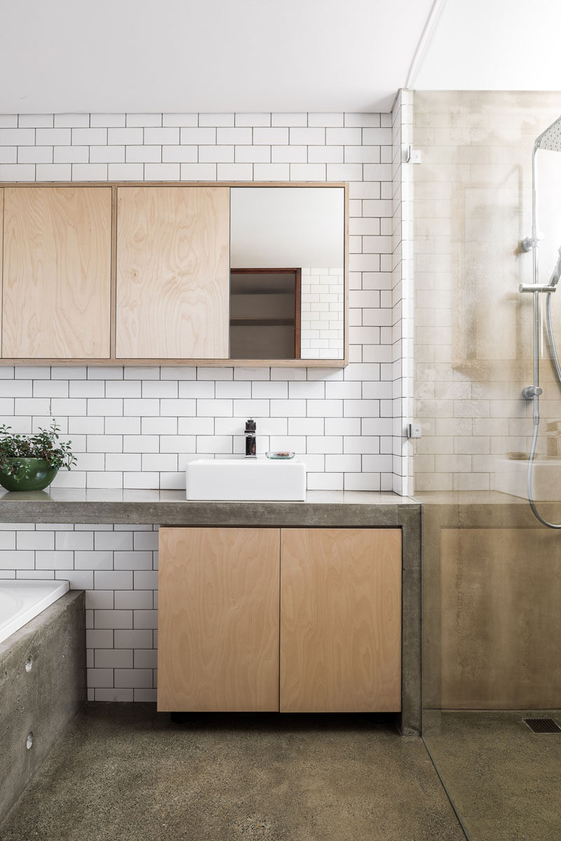 This modern bathroom features concrete counters and a concrete bathtub surround. White subway tiles and light wood cabinetry help to keep the bathroom bright. #BathroomDesign #ModernBathroom #Concrete