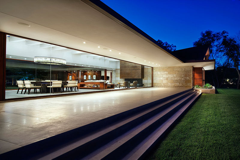 At the rear of this modern house, the large glass walls look out onto a patio that leads down to the backyard. #GlassWalls #Patio #CoveredPatio #Architecture