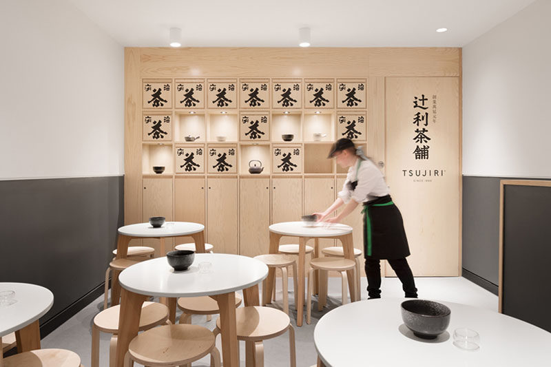 This modern Japanese tea house has built-in wood display shelves, that are decorated with traditional Japanese tea boxes, while small round tables with stools provides seating for guests. #TeaHouse #ModernCafe #WoodShelving