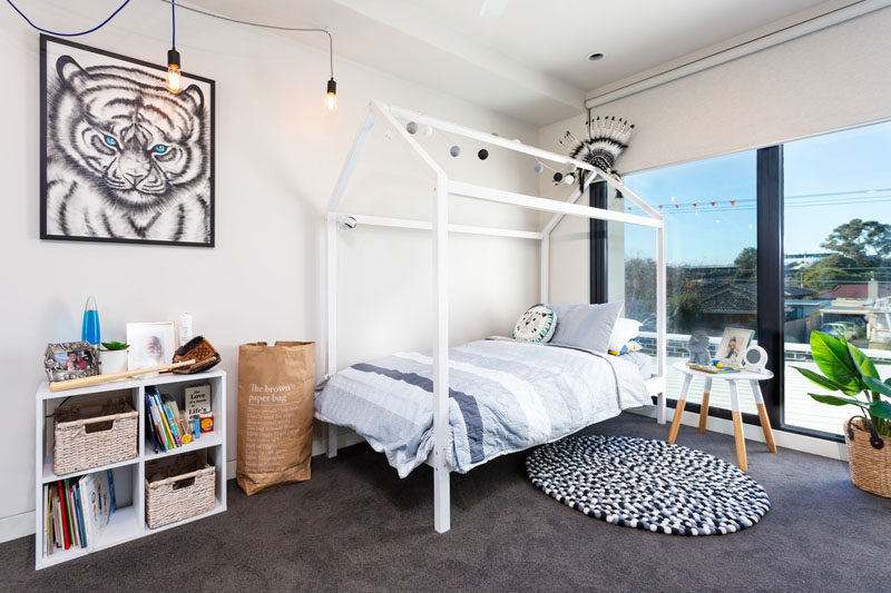 In this children's bedroom, large windows flood the room with natural light, and a dark carpet contrasts the light colored walls. #BedroomDesign #ChildrensBedroom