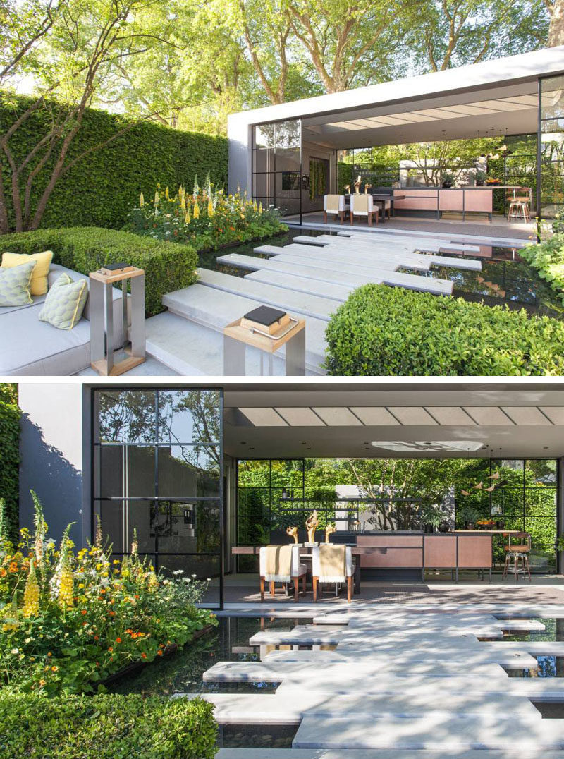 The stone steps from a sunken patio/lounge area transform into wide rectangular stepping stones that are surrounded by water, and lead to a pavilion with a dining area and kitchen. #Landscaping #LandscapeDesign #ModernGarden #GardenPavilion