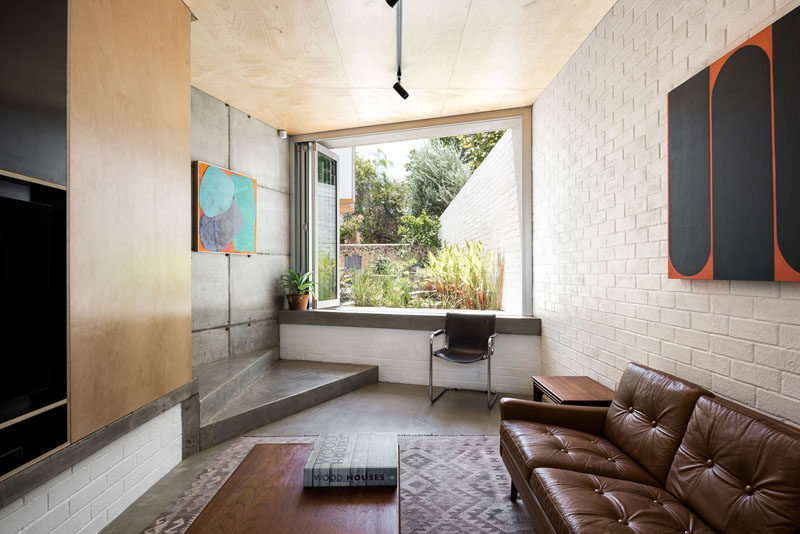 This small living room features a white brick wall, and folding windows that can be opened to provide a view of the garden. #LivingRoom #FoldingWindows