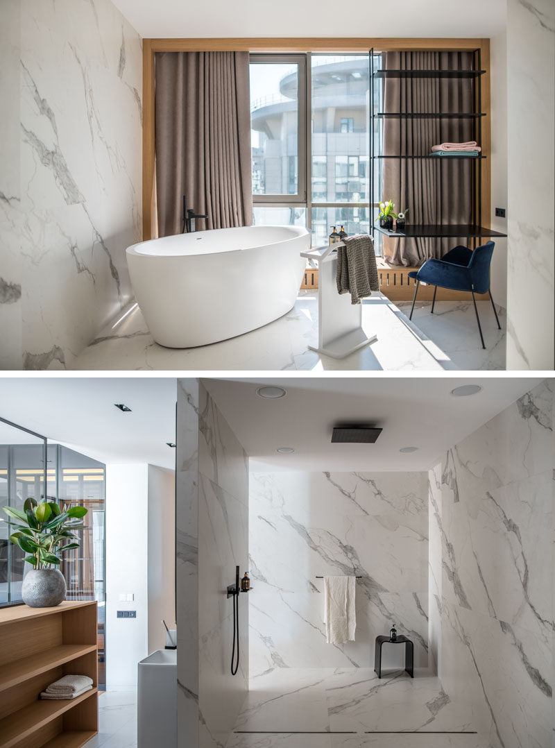 White marble tiles covering the walls and floor of this modern bathroom, while a freestanding bathtub sits in front of the window. Behind it is an open shower. #BathroomDesign #MasterBathroom #ModernBathroom