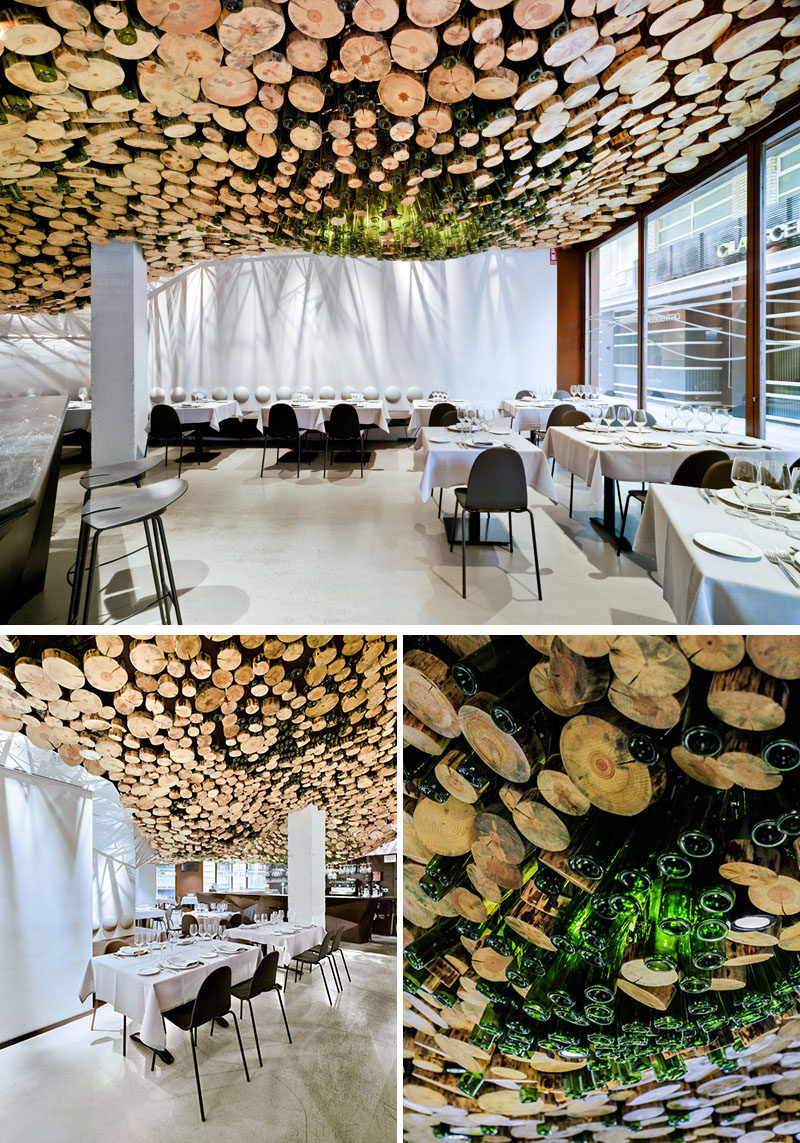 A wavy installation of cut logs and green glass cover the ceiling of this modern restaurant. #Ceiling #Restaurant #RestaurantDesign #InteriorDesign