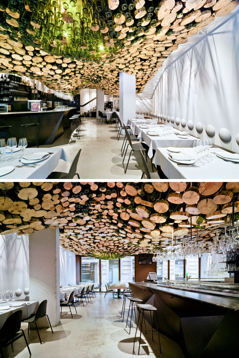 A wavy installation of cut logs and green glass cover the ceiling of this modern restaurant. #Ceiling #Restaurant #RestaurantDesign #InteriorDesign
