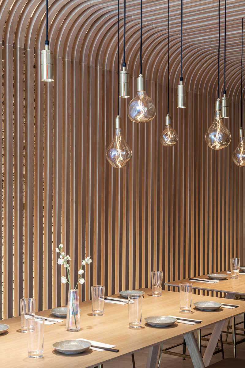 Lining the walls and ceiling is a wood slat screen that resembling the rice noodle featured in this modern restaurant. #WoodSlats #WoodScreen #Restaurant #RestaurantDesign #Interiors