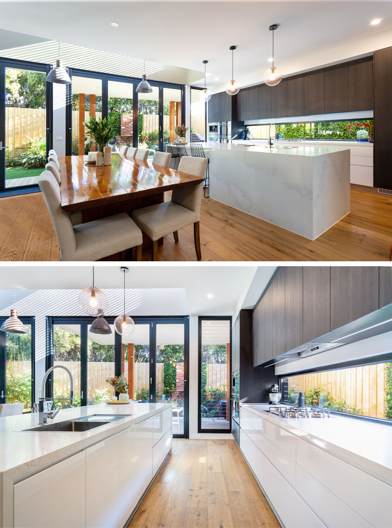 This modern kitchen has a long horizontal window that looks out to the garden at the side of the house, while the dark wood cabinets contrast the light island and lower cabinets. #ModernKitchen #KitchenDesign