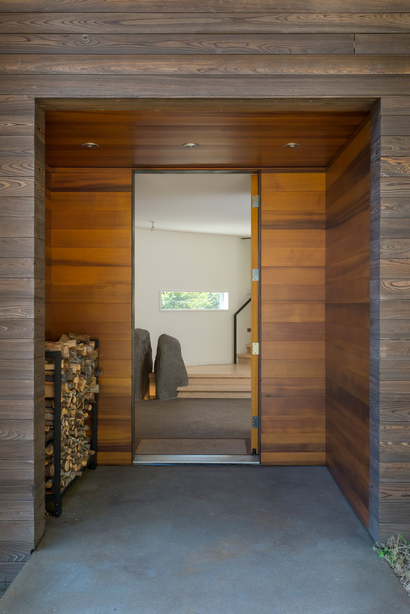 The wooden front door of this modern is set back from the facade, and the alcove provides a place to keep firewood dry. #Entryway #FrontDoor #FirewoodStorage