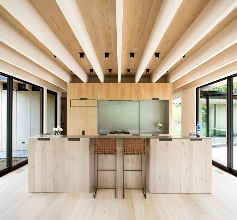 This minimalist kitchen features wood cabinets that match the wood used in the construction of the house, while a large island creates additional storage, and a place for a couple of people to sit at. #KitchenDesign #ModernKitchen #WoodKitchen