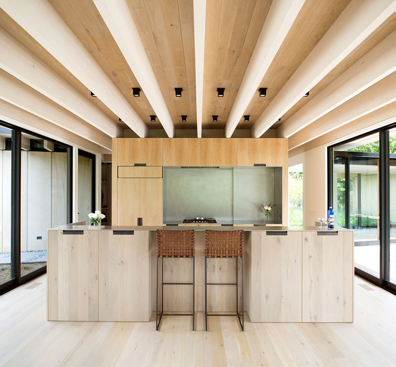 This minimalist kitchen features wood cabinets that match the wood used in the construction of the house, while a large island creates additional storage, and a place for a couple of people to sit at. #KitchenDesign #ModernKitchen #WoodKitchen