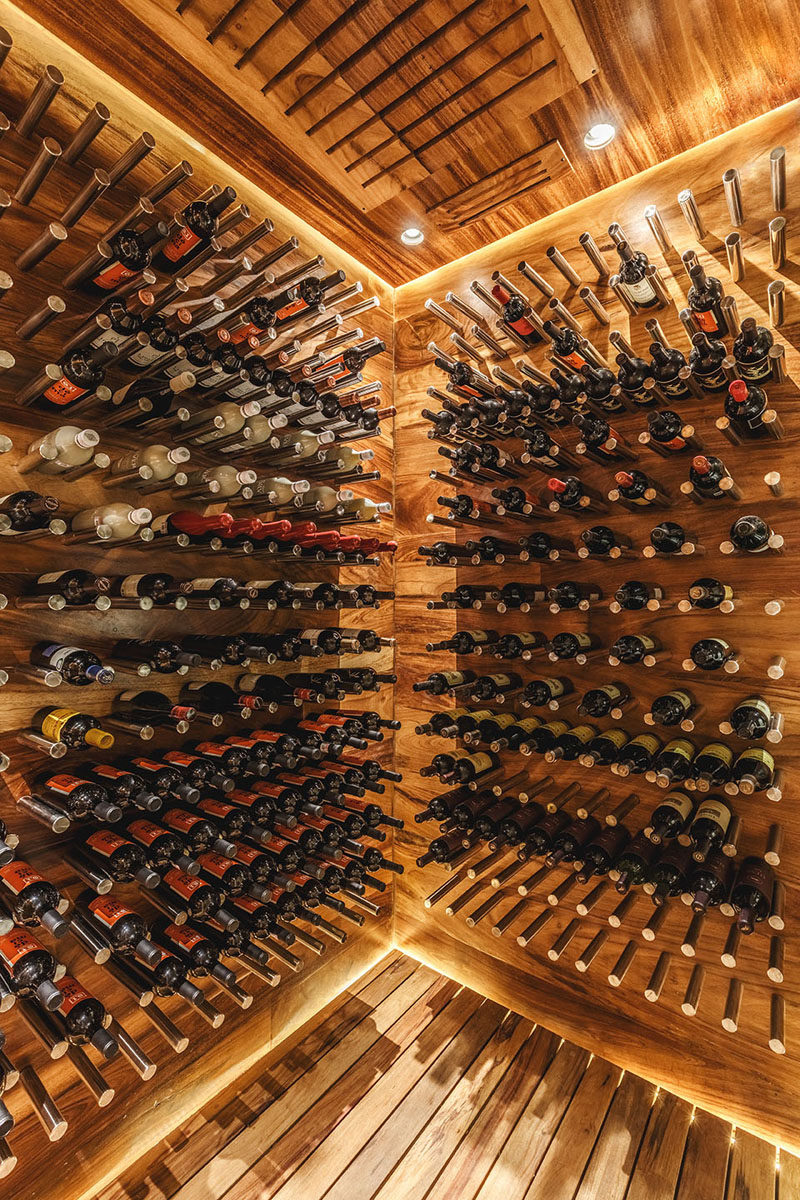 This modern wood covered wine cellar uses metal rods to create exposed shelving for the wine, showing off the home owners collection. #WineCellar #WineStorage