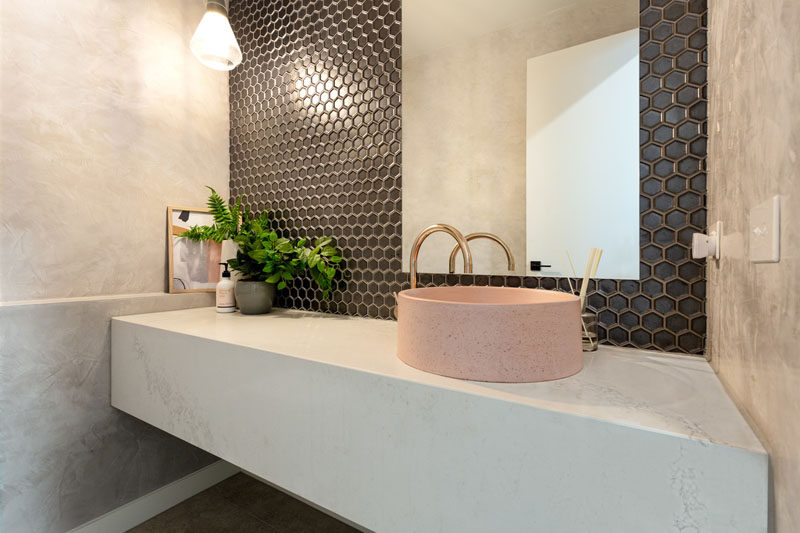 In this modern powder room, dark hexagonal tiles cover the wall, while a dusty pink round basin sits on a floating white vanity. #PowderRoom #Bathroom