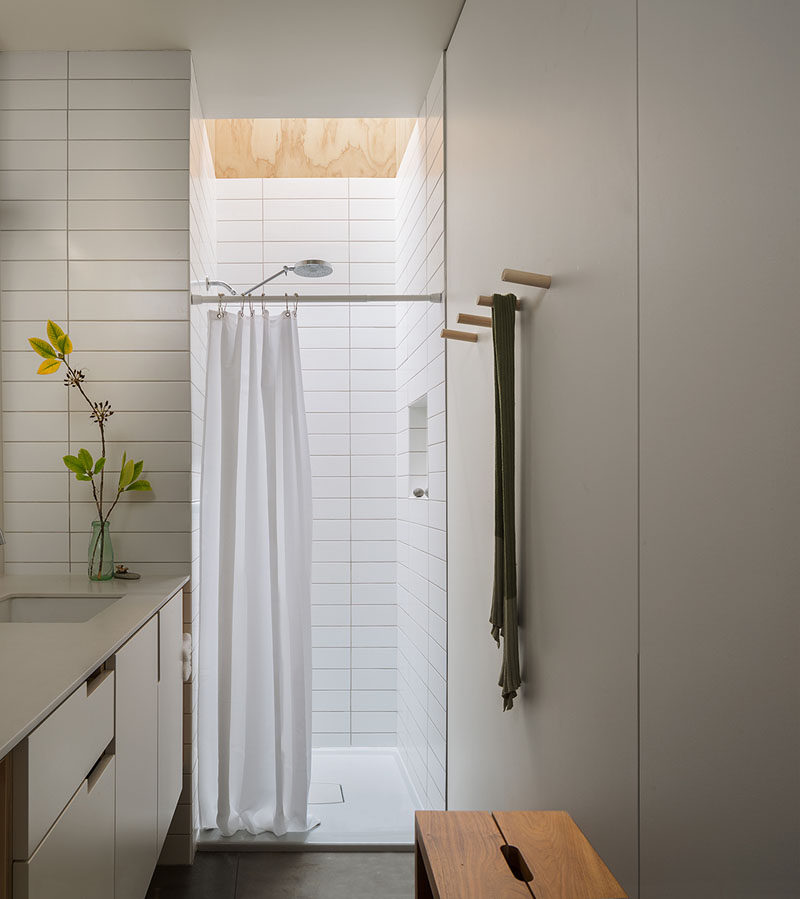 This modern and small bathroom has a skylight above the show, while long rectangular white tiles line the shower and wrap around to the vanity area. #BathroomDesign #BathroomSkylight #SmallBathroom #WhiteBathroom