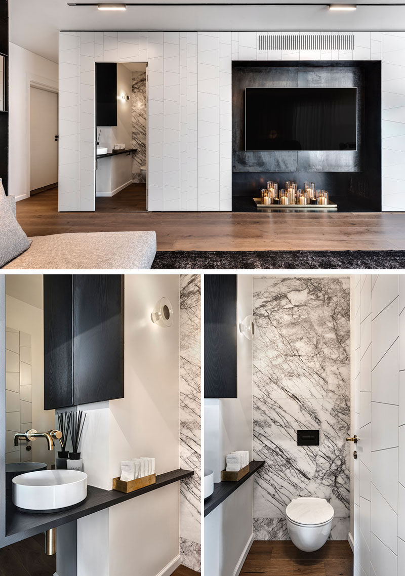 This small powder room has grey and white marble that lines the back wall, while a simple black wood vanity fits against the adjacent wall. #PowderRoom #ModernInterior #SmallBathroom