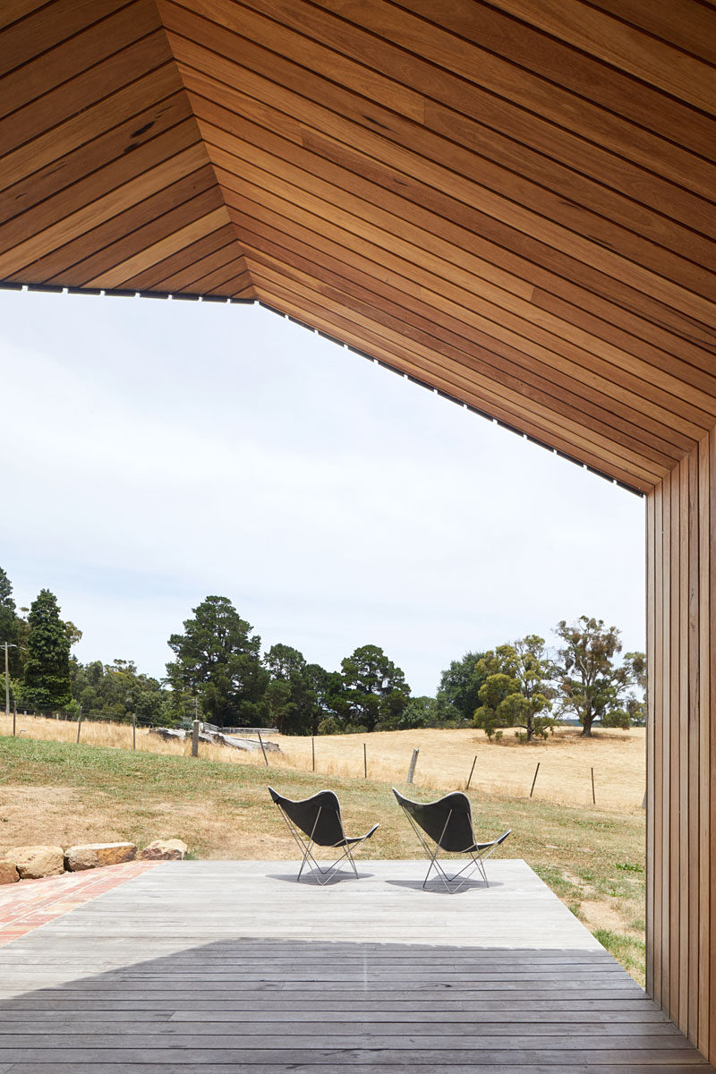 The deck of a modern house addition, which is partially covered by the gabled form, extends away from the dining area, and connects to brick patio. #OutdoorSpace #Architecture