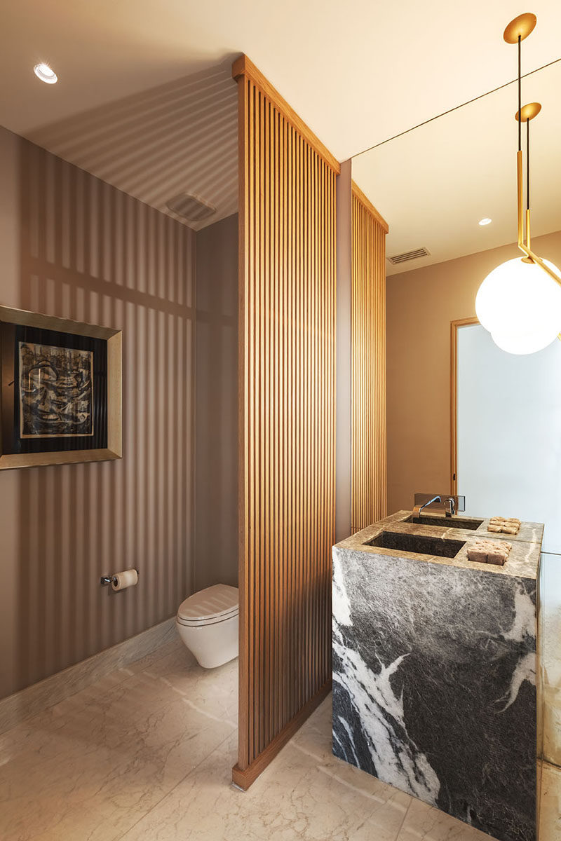 In this modern powder room, a wood slat wall separates the vanity area from the toilet, without blocking the light from the pendant light. #WoodSlatWall #PowderRoom #ModernBathroom
