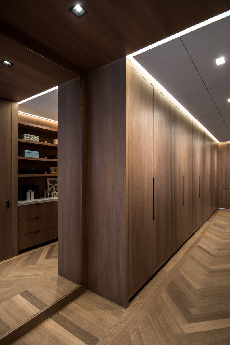 This modern walk-in closet has minimalist oak paneling and doors, and a floor to ceiling mirror reflects the light throughout the space. #Closets #InteriorDesign #WoodFlooring