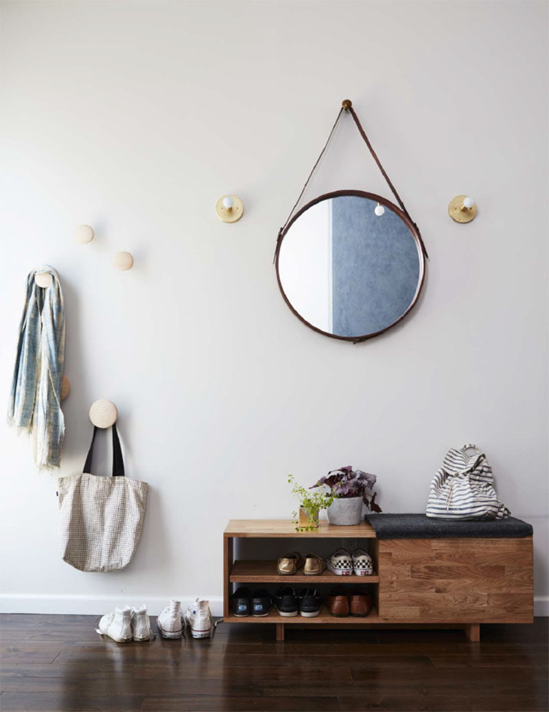 In this contemporary entryway, a round mirror is flanked by sconces, while round hooks provide a place to hang jackets and bag, and a wood bench allows to storage of shoes. #Entryway #InteriorDesign